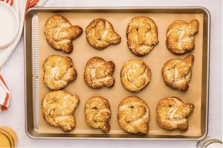 Homemade sourdough starter discard pretzels sitting on a sheet pan cooling, topped with butter and salt.