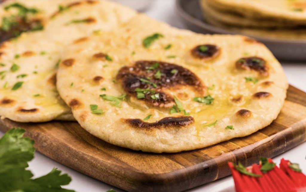 Sourdough starter discard naan sitting on a cutting board with parsley garnished on top, ready to be enjoyed.