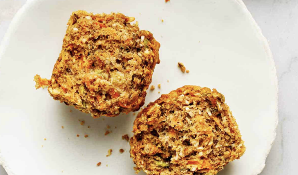 Sourdough starter discard hearty muffin cut in half on a white plate. The muffin is packed with minced nuts and grains, ready to be enjoyed.