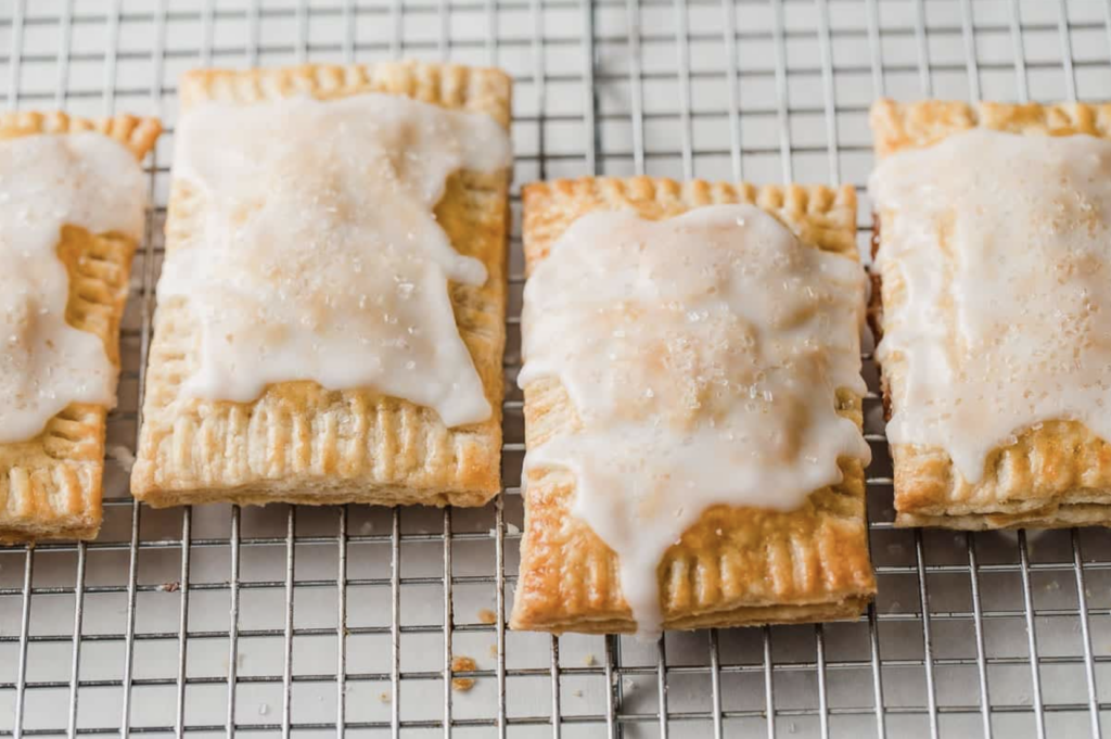 Sourdough starter discard pop tarts sitting on a cooling wrack in a line of four, with white drizzle melted and falling off the sides; topped with sugar crystals.