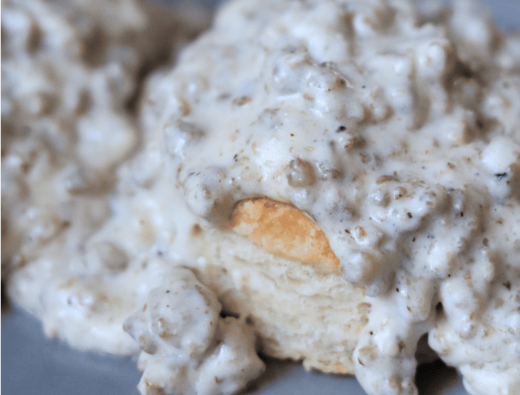 Sourdough sausage gravy thickened with sourdough starter discard. Gravy is poured perfectly over homemade sourdough starter discard bisuits.