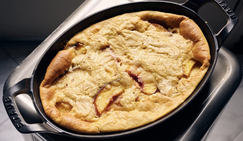 Sourdough starter discard clafoutis with peaches in an oval cast iron dish ready to be enjoyed.