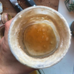 close up image of woman holding glass jar of sourdough starter with hooch on the top