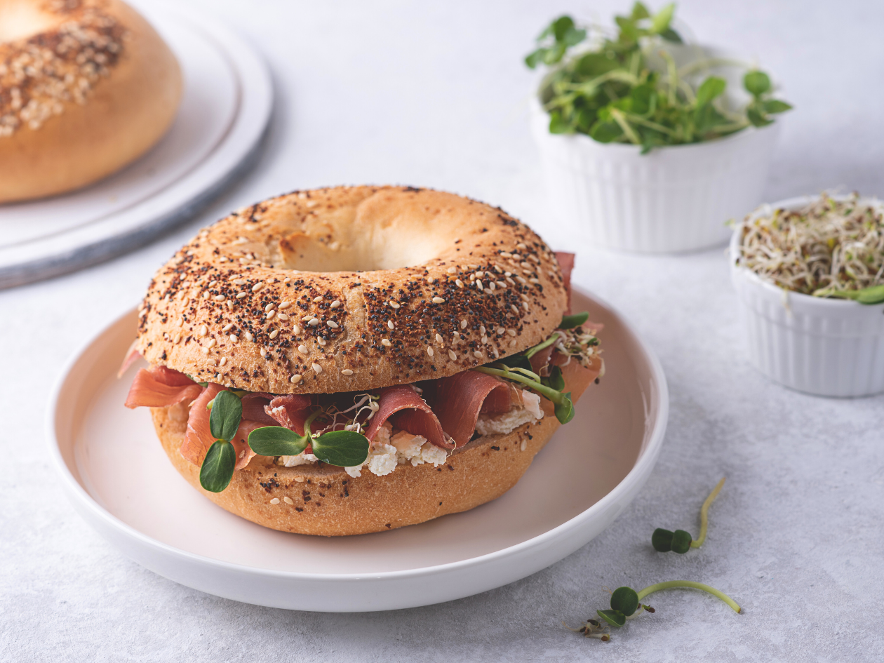 bagel with meat, cream cheese and microgreens placed on a white plate