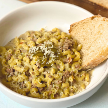 One-Pot Cheeseburger Pasta in a white bowl with a slice of sourdough bread on a white countertop