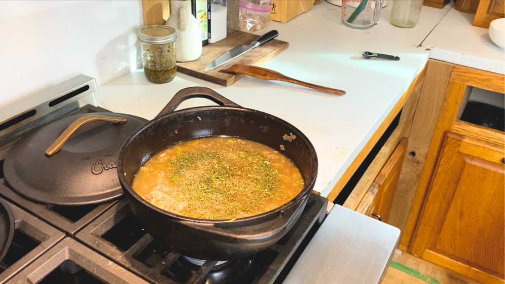 one-pot cheeseburger chowder in a cast iron dutch oven with spices sprinkled on top about to be mixed in