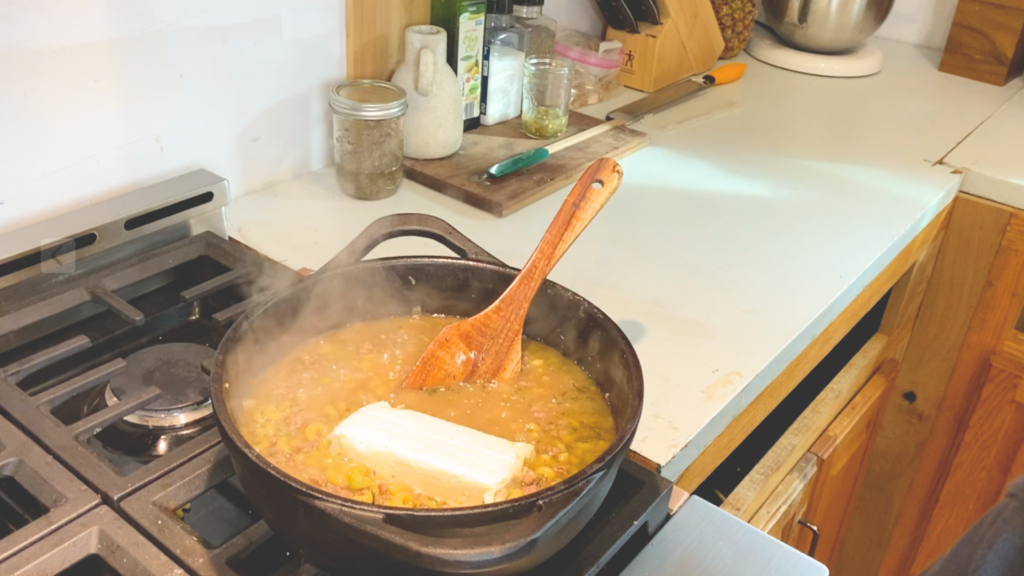 One-pot cheeseburger pasta cooking in a cast iron dutch oven with 8oz of cream cheese just added about to be mixed in