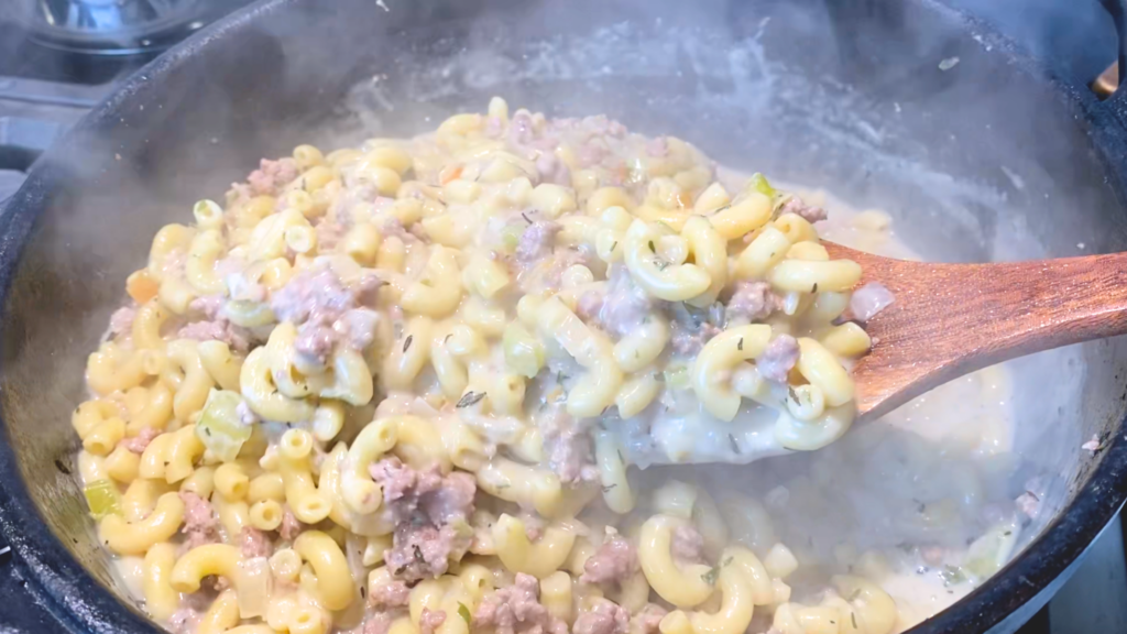 Close up of one-pot cheeseburger pasta in cast iron dutch oven with a wooden utensil scooping some out to be dished up