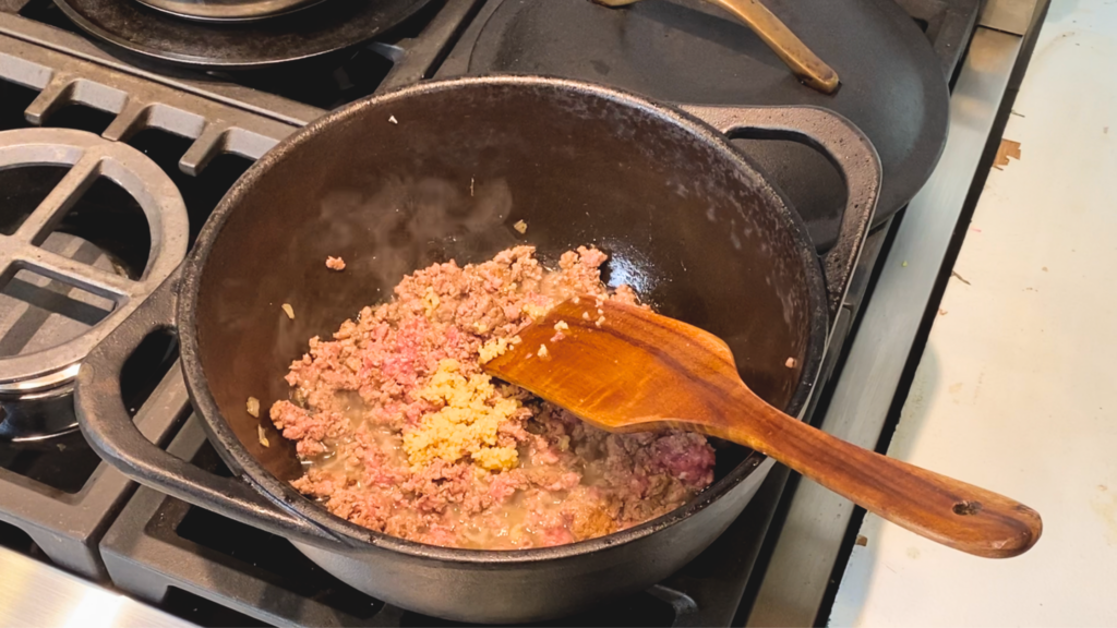 Browning ground pork in a cast iron dutch oven with minced garlic